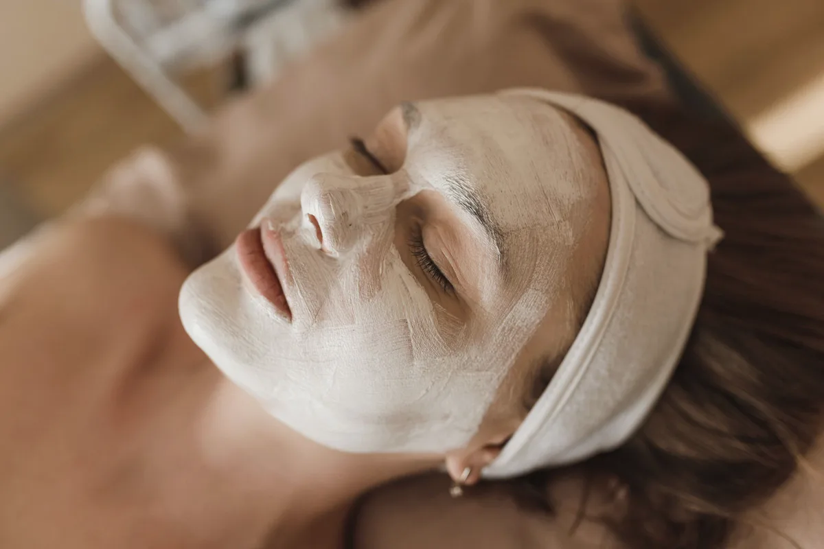 A client resting with a white treatment mask on her face and a cloth headband